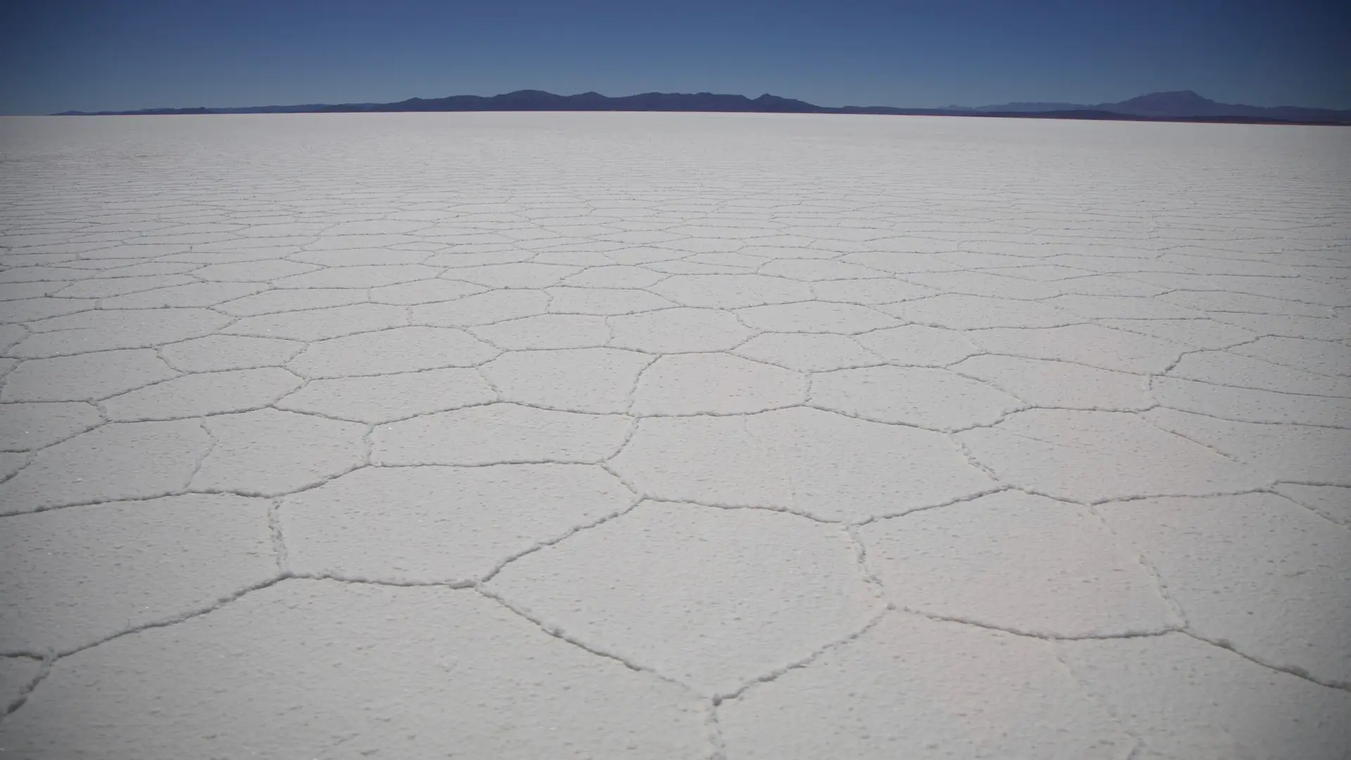 The white hexagonal salt polygons of the Salar de Uyuni stretching to distant mountains under a clear blue sky